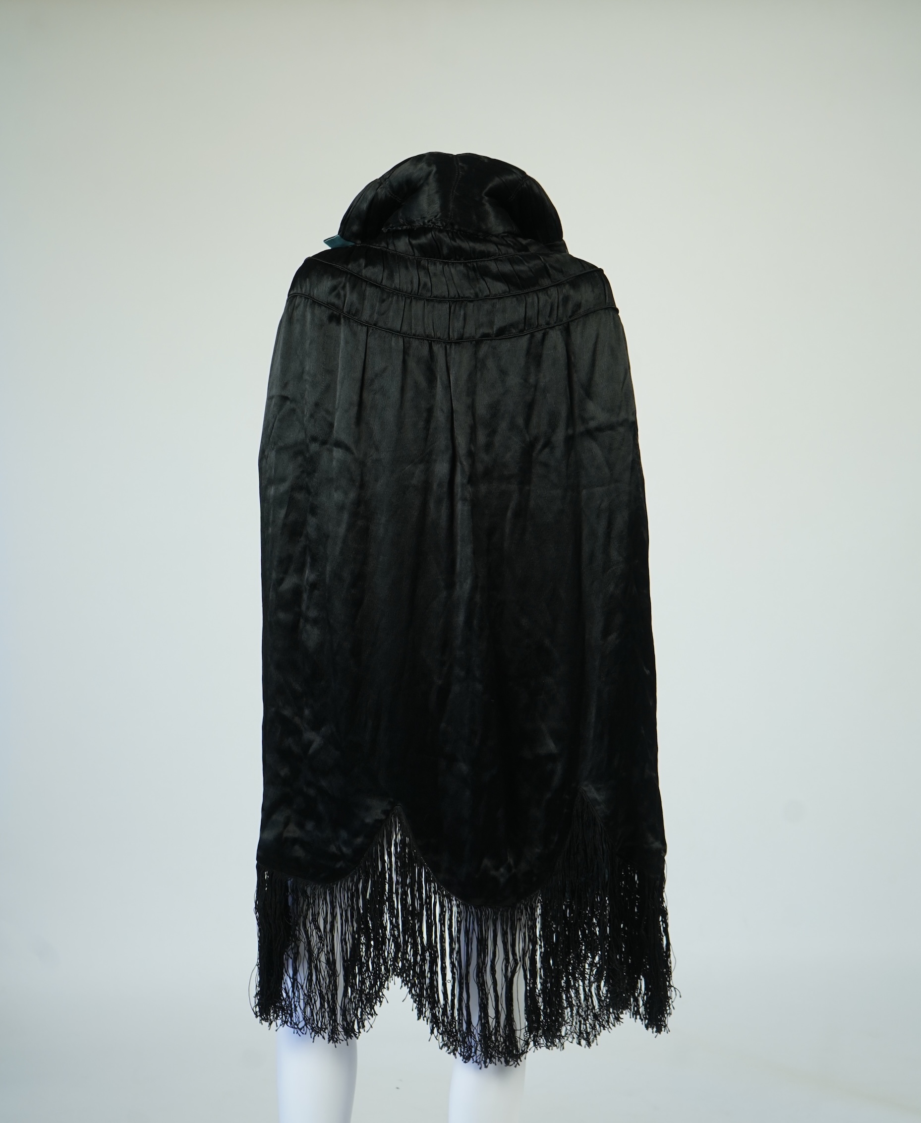 A 1920's ladies blue lined, black silk opera cape. Designed with a rushed ornate collar and scalloped and fringed lower edge. 95cm long fron neck to base. Condition - stained near the front edge, possibly removable with